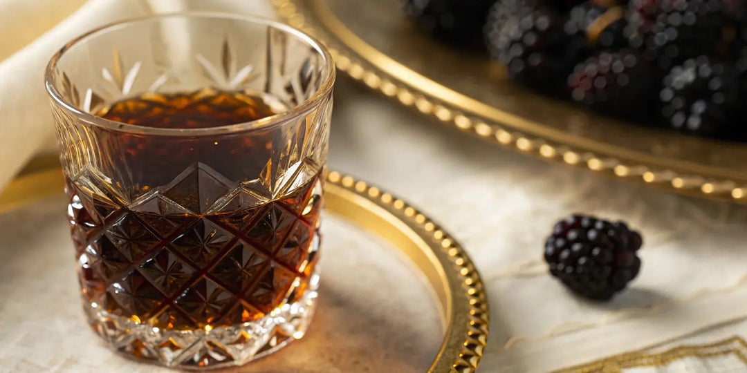 A glass of Crown Royal Blackberry whisky garnished with fresh blackberries on a tray.