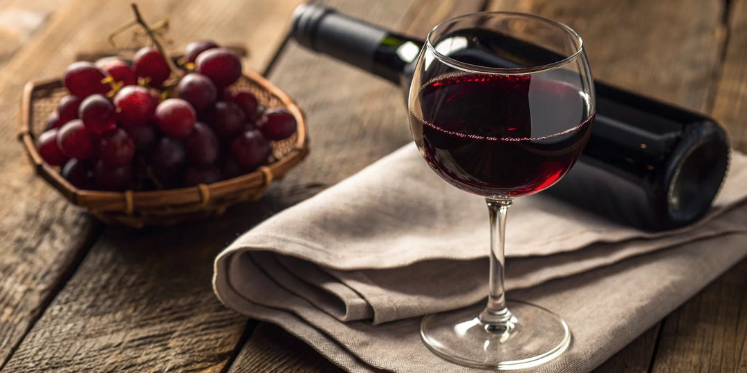 A glass and bottle of Decoy Cabernet Sauvignon with grapes on a wooden table.