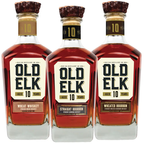 Three bottles from the Old Elk 10 Year Series Bundle—Bourbon Whiskey, Wheated Bourbon Whiskey, and Wheat Whiskey by Old Elk Bourbon—are arranged side by side against a white background, each showcasing rich amber liquid and wooden-topped corks.