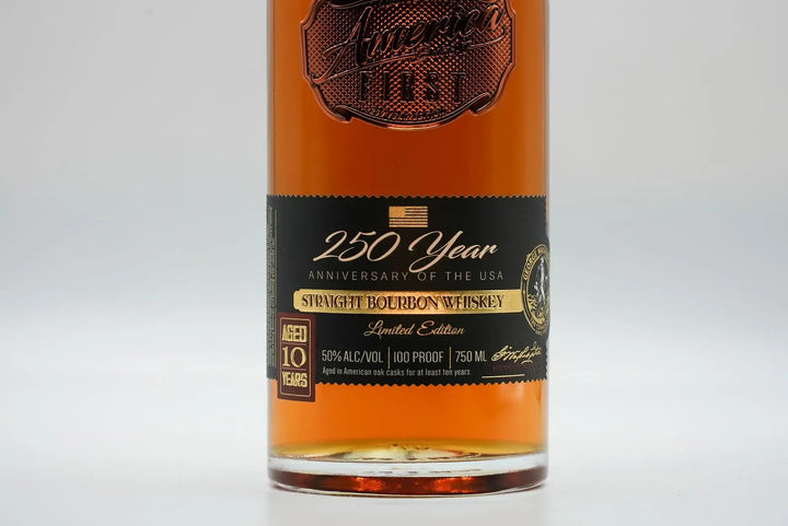 A close-up of a whiskey bottle label reads “America First 250 Year Limited Edition Bourbon, Straight Bourbon Whiskey, 10 Years Old, 50% Alc/Vol, 100 Proof, Limited Edition Bourbon, 750 mL.”.