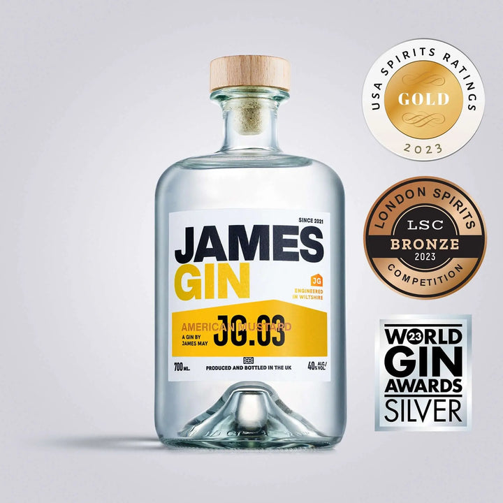 A clear 700mL bottle of James Gin American Ramstud with a wooden cap and striking yellow-blue label is shown, alongside three award badges (Gold, Silver, Bronze) and a souvenir gift key chain.