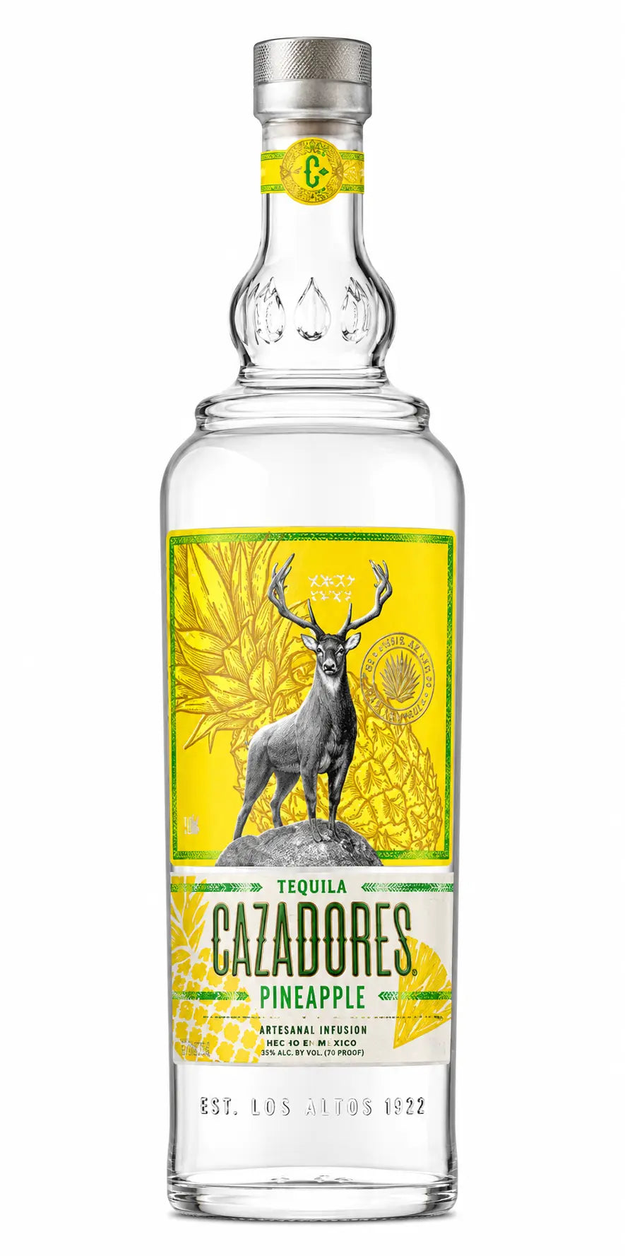 A clear glass bottle of Cazadores Tequila's Pineapple Tequila, featuring a yellow label with a black and white stag illustration, a pineapple in the background, and a silver cap with a green accent.