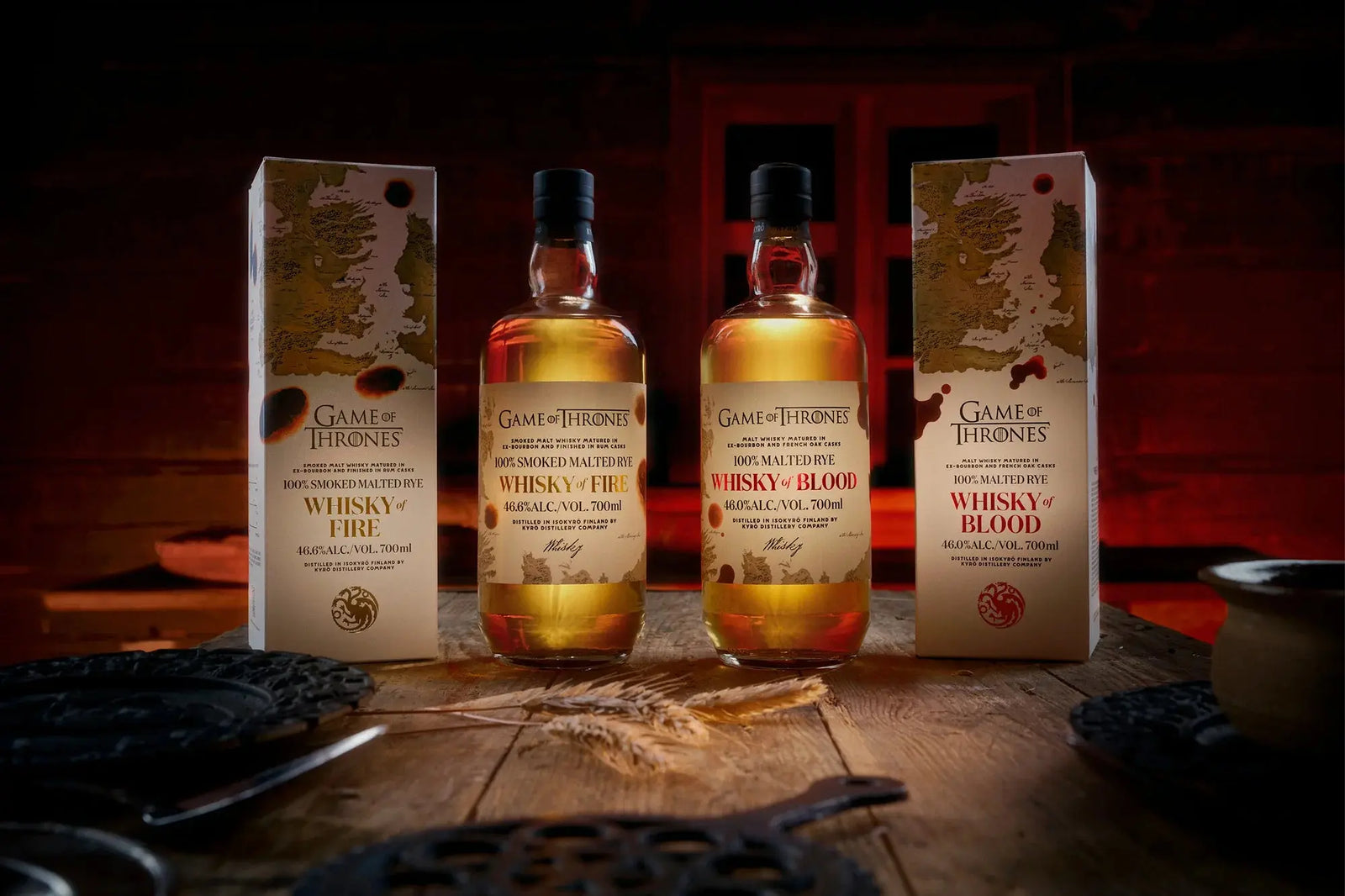 Three bottles of the Kyrö x Game of Thrones Whisky of Fire & Blood Bundle (PRE-ORDER) from Main Street Liquor stand between matching boxes on a rustic wooden table, set against a dramatic, red-lit backdrop.