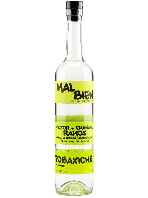 A tall, clear bottle of Mal Bien Tobaxiche Ramos mezcal from Miahuatlán, Oaxaca with a yellow label featuring the brand name Mal Bien and artisanal mezcal details in bold black text.