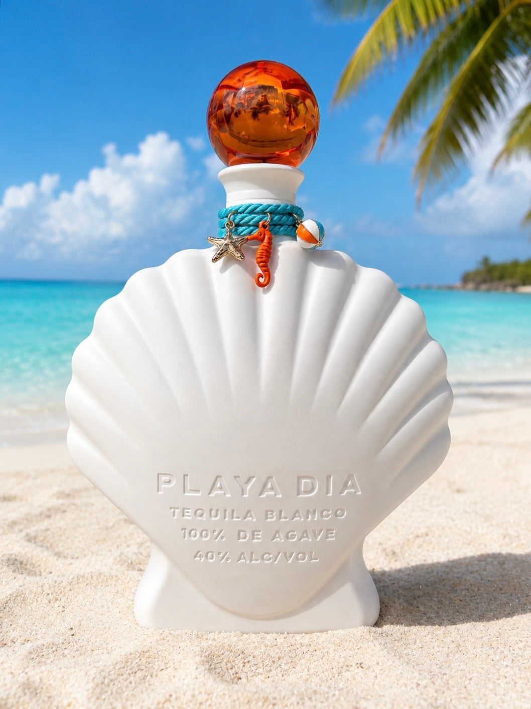 A shell-shaped bottle of PLAYA DIA Blanco Tequila with an orange cap rests on a sandy beach. The label reads “Playa Dia Blanco Tequila, 100% de Agave, 40% Alcohol.” In the background, palm trees and the ocean set the scene for this additive-free tequila, crafted exclusively from 100% Blue Weber agave.