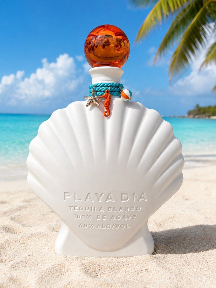 A shell-shaped bottle of PLAYA DIA Blanco Tequila with an orange cap rests on a sandy beach. The label reads “Playa Dia Blanco Tequila, 100% de Agave, 40% Alcohol.” In the background, palm trees and the ocean set the scene for this additive-free tequila, crafted exclusively from 100% Blue Weber agave.