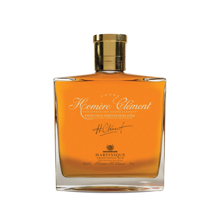 A square glass bottle of Rhum Clément Cuvée Homère features gold liquid, a gold cap, and elegant gold and white lettering on the label.