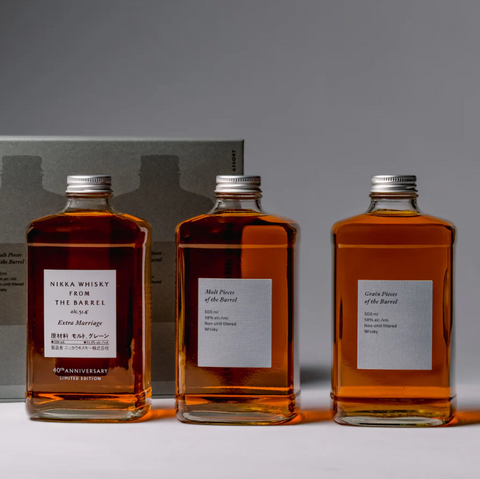 Three rectangular bottles of Nikka whisky—including the 40th Anniversary Limited Edition—stand side by side before a gray box in the Nikka From The Barrel Extra Marriage Gift Set, an eye-catching Japanese collector’s item with glowing amber tones.