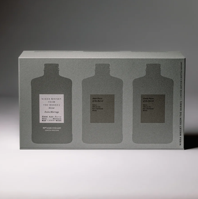 A rectangular gray box labeled "Nikka From The Barrel Extra Marriage Gift Set" by Nikka features silhouettes of three bottles, with extra detail on the center one. Soft lighting casts gentle shadows behind this Japanese whisky collector’s set.