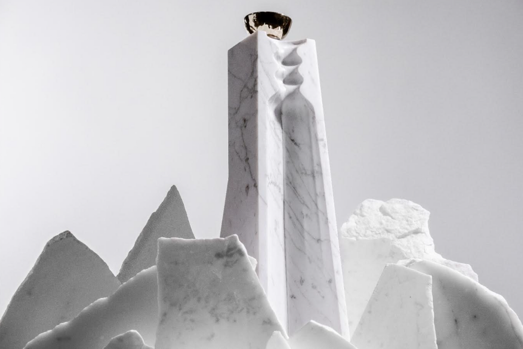 A tall, white marble sculpture with graceful curves and a metallic cup reflects the elegance of Volcan De Mi Tierra Coleccion I Hacienda La Gavilana Anejo Tequila, its refined form highlighted against a light backdrop.