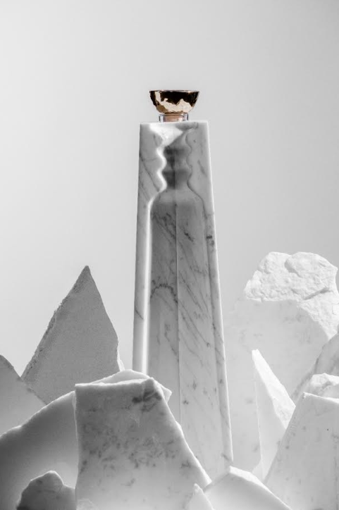 A tall, white marble Volcan De Mi Tierra Coleccion I Hacienda La Gavilana Anejo Tequila bottle with a gold cap stands amid jagged white stones on a light gray background, casting a subtle shadow and exuding refined elegance.