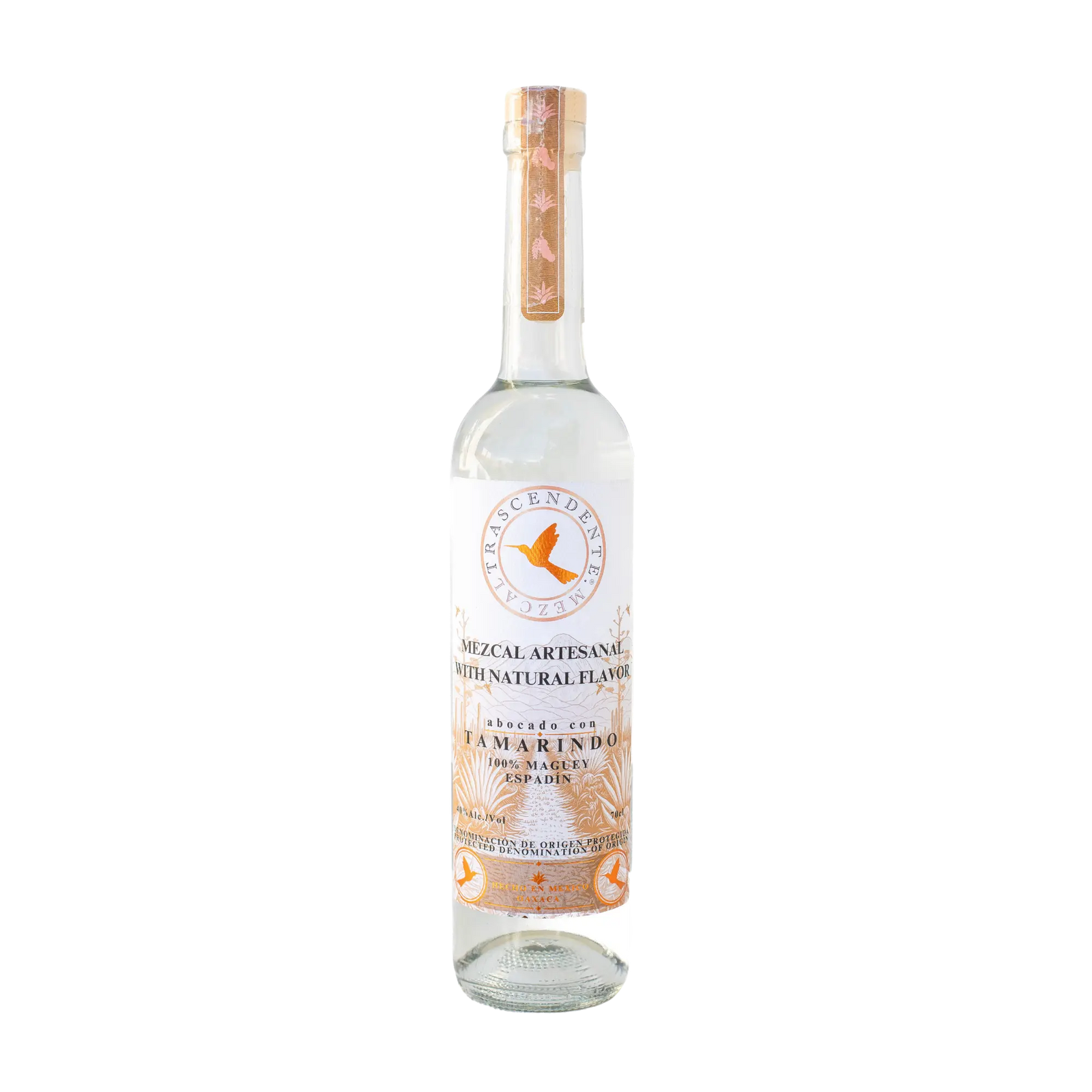 A clear glass bottle of Mezcal Trascendente Tamarindo 700ml by Mezcal Trascendente, with a white label, gold accents, wooden cap, decorative base design, and natural tamarind flavors made from Espadín mezcal.
