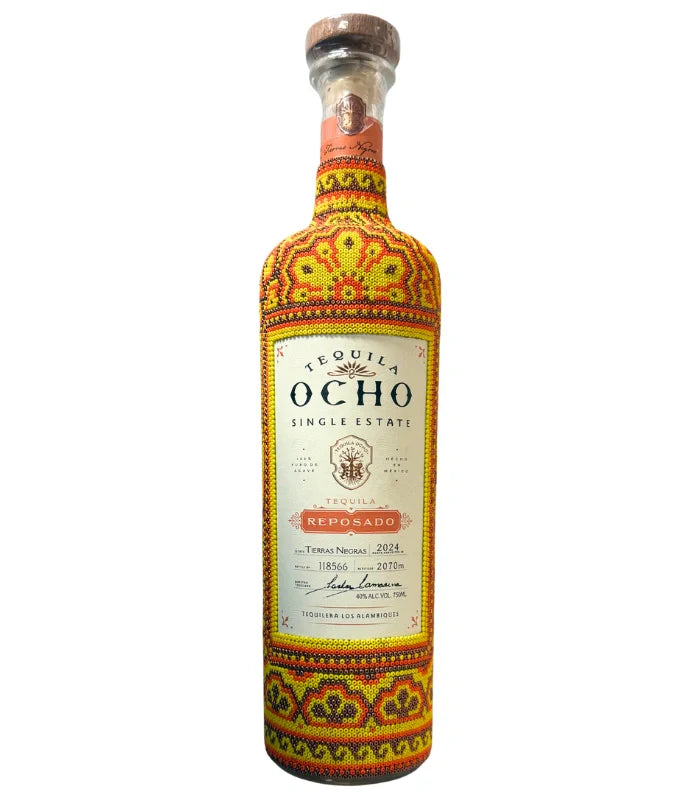 The Ocho Tequila Reposado Huichol Art Edition features colorful red, yellow, and orange beadwork patterns covering the bottle except for the label and neck.