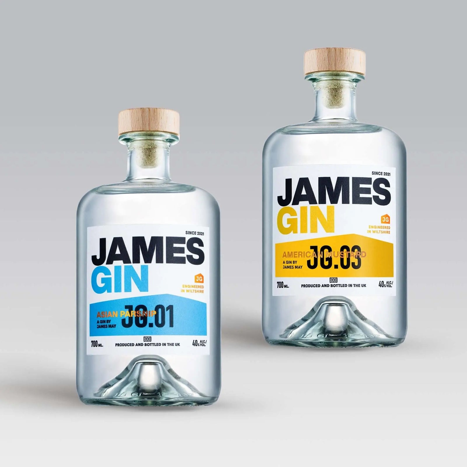 Two clear James Gin US bottles from the James Gin The Hedge 2 Bottle Bundle with wooden caps and labels—one blue-accented “Asian Parsnip 00:01,” one yellow “American Mustard 00:03”—are displayed with a souvenir gift key chain.