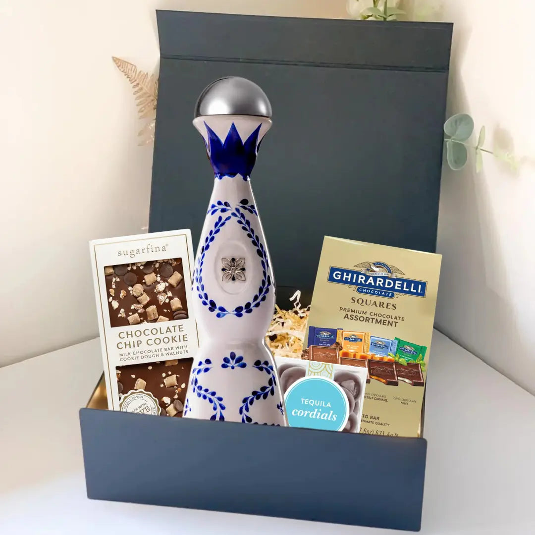The Premium Tequila Gift Box from Main Street Liquor includes a blue and white ceramic bottle of premium tequila, Sugarfina chocolate chip cookie bites, Ghirardelli chocolate squares, and a small box of tequila cordials.