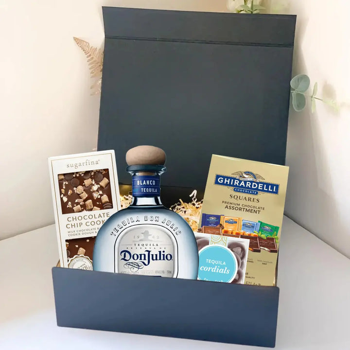The Premium Tequila Gift Box by Main Street Liquor includes Don Julio premium tequila, Ghirardelli gourmet chocolate, Sugarfina chocolate chip cookie candies, and tequila cordials, all elegantly arranged with decorative filler.