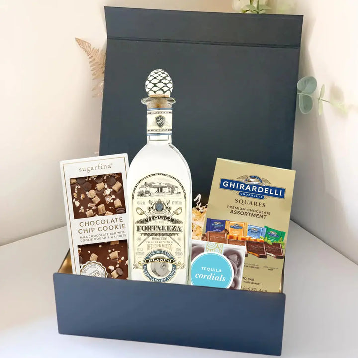 The Premium Tequila Gift Box from Main Street Liquor features Fortaleza tequila, Sugarfina chocolate chip cookie bites, and Ghirardelli chocolate squares, all beautifully arranged against a light background.