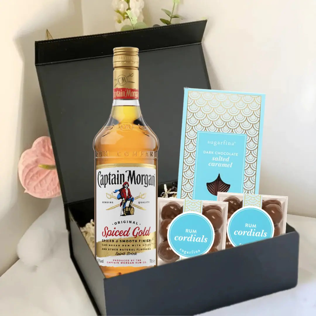 The Premium Rum Gift Box by Main Street Liquor includes Captain Morgan Spiced Gold, Sugarfina Rum Cordials, and dark chocolate sea salt caramels, elegantly presented against a light background.