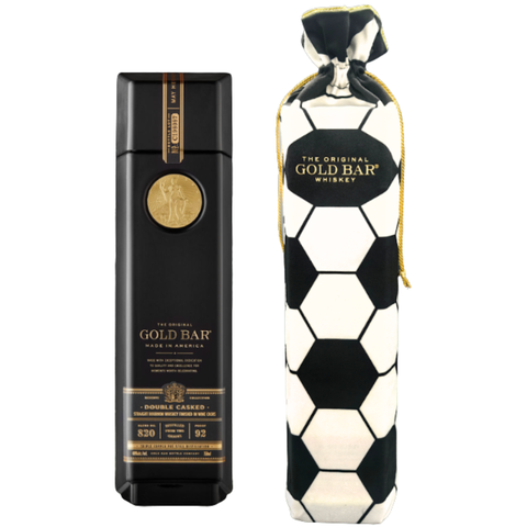 A black and gold bottle of Gold Bar Black Double Cask Bourbon Soccer Bag Edition stands beside a soccer bag edition fabric bag with a gold drawstring, both branded Gold Bar and showcasing this unique double cask bourbon.