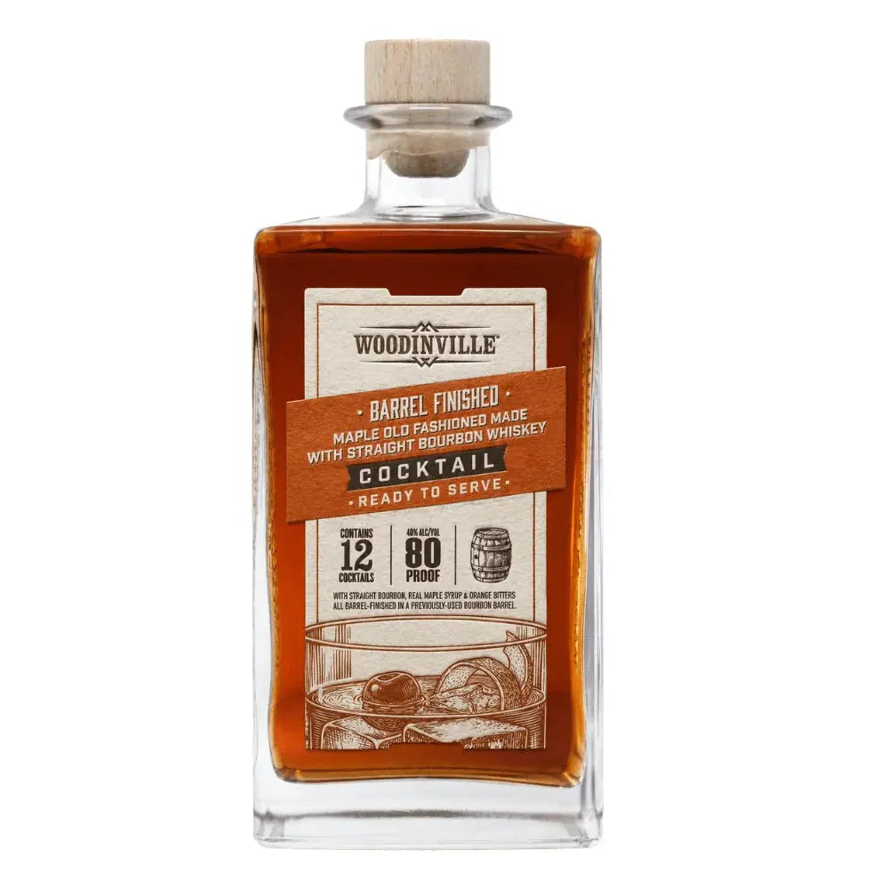 A rectangular glass bottle of Woodinville Barrel-Finished Maple Old Fashioned Ready-to-Serve Cocktail from Woodinville, a bourbon whiskey cocktail with a wooden cap and brown label featuring product details, whiskey illustrations, 80 proof strength, and information indicating it contains 12 ready-to-pour Old Fashioned cocktails.