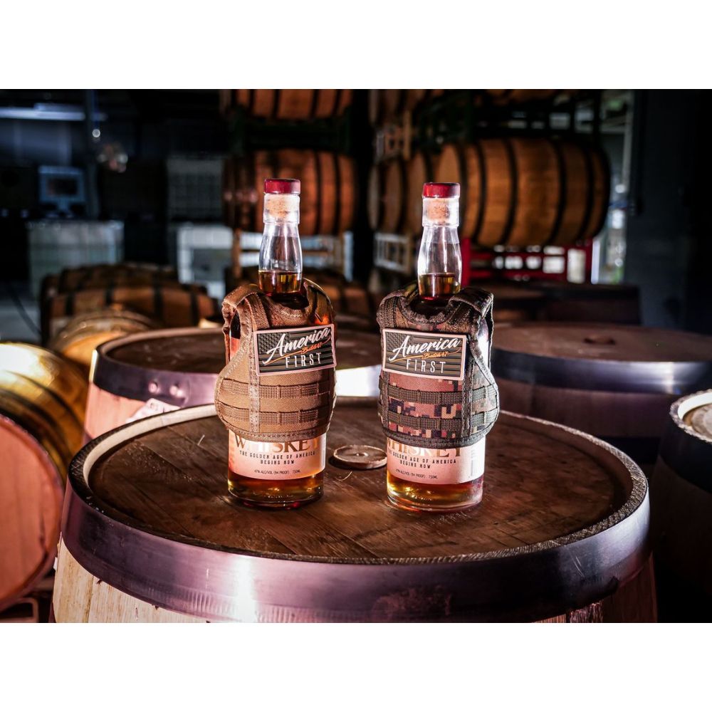 Six bottles of America First Straight Bourbon Whiskey from the America First brand are showcased on a wooden barrel, set within a distillery lined with aging Kentucky bourbon barrels in the background.