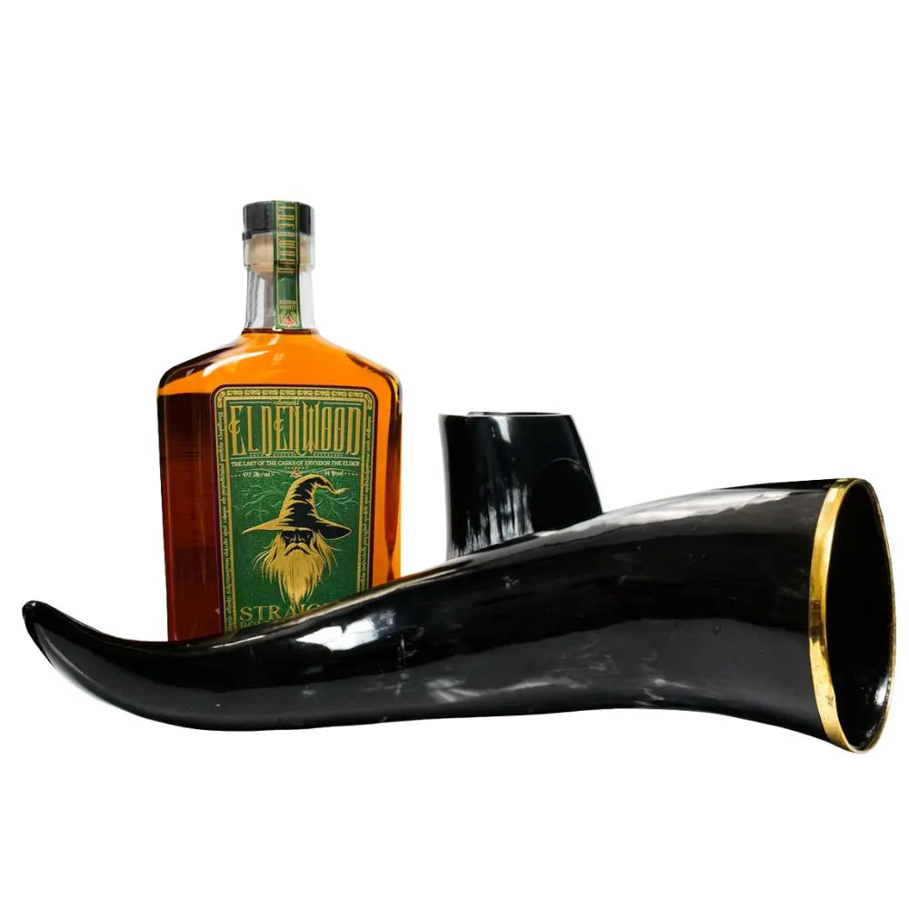 A bottle of Eldenwood Straight Bourbon Whiskey by Eldenwood with a green label featuring Eryndor the Elder, displayed beside a large polished black drinking horn with a gold-trimmed rim.