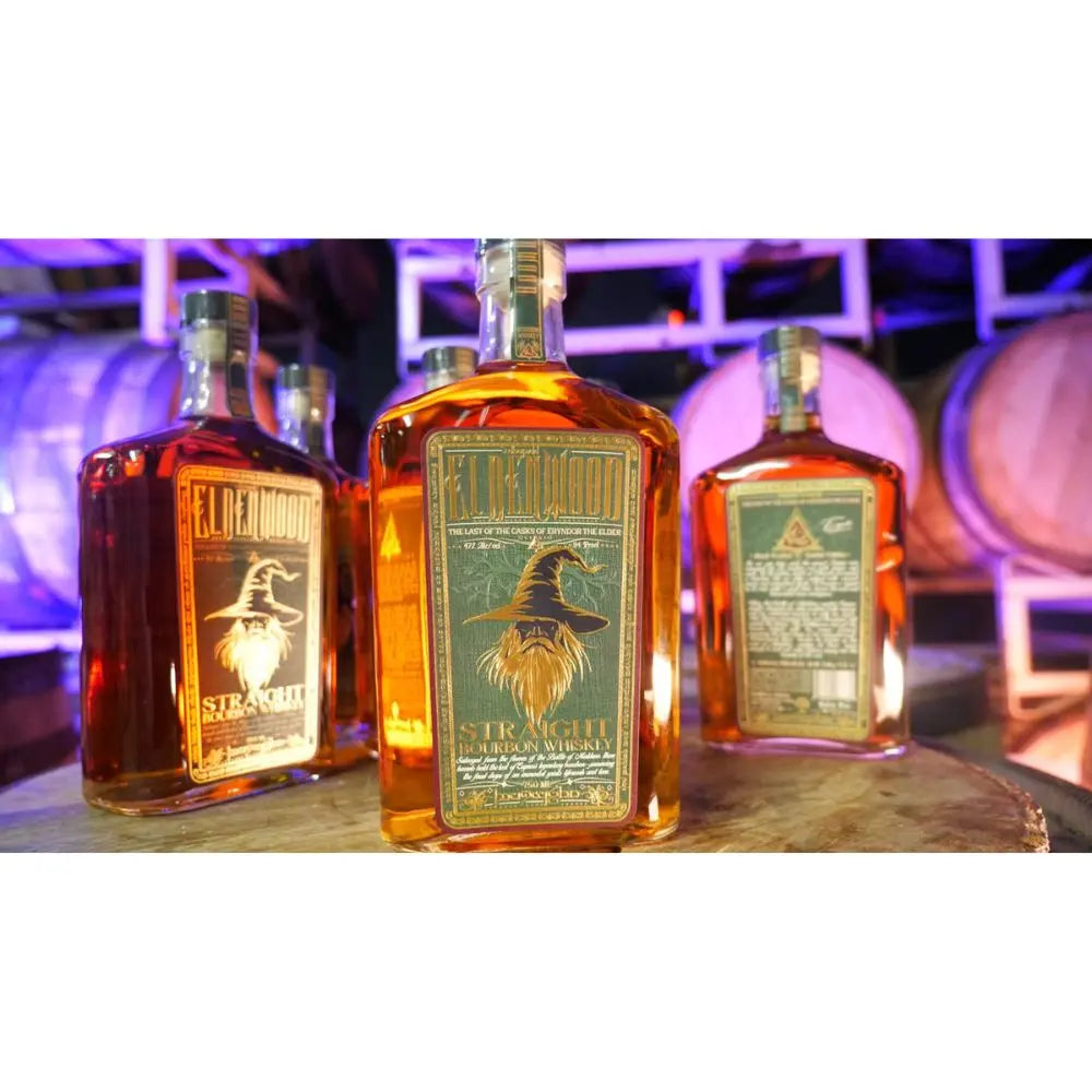 Three bottles of Eldenwood Straight Bourbon Whiskey 3 Pack sit on a barrel, with barrels behind and purple lighting. Each bottle from Eldenwood features a bearded wizard illustration on the label.
