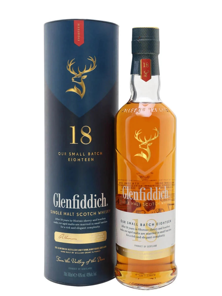 A bottle of Glenfiddich 18 Year Single Malt Scotch Whisky stands next to its matching box, both featuring the gold stag logo and branding, highlighting the amber spirit inside the clear glass.