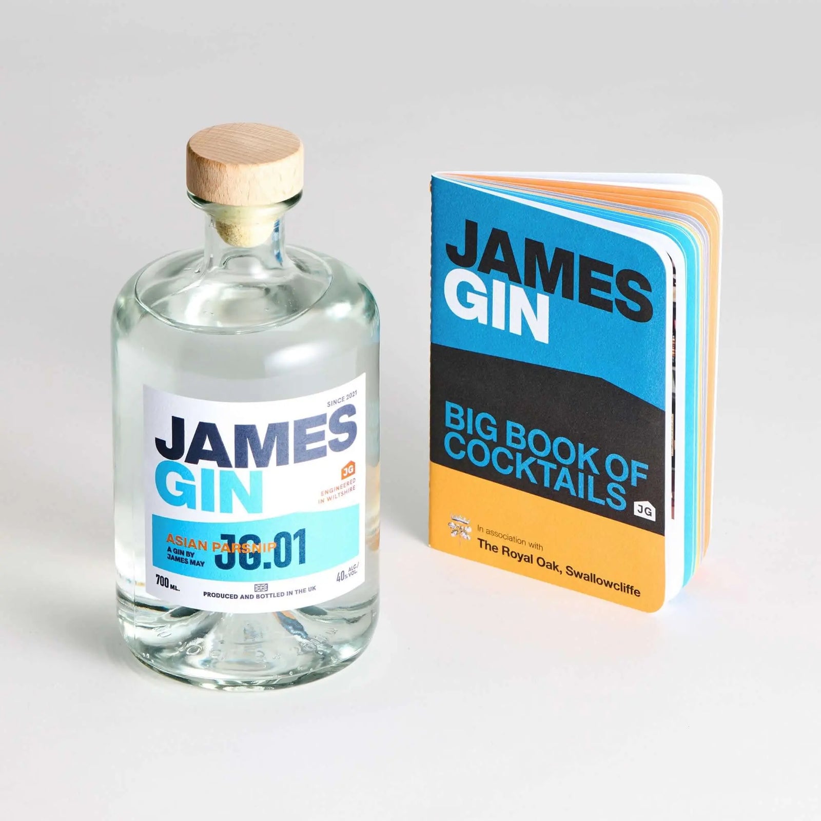 The James Gin US Impressive Cocktail Kit, featuring a bottle with wooden cap, the “James Gin Big Book of Cocktails,” and a souvenir key chain, stands out with bold blue and orange designs against a plain background.