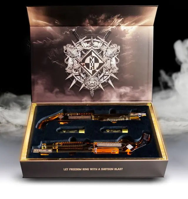 A decorative collectors box with ornate artwork holds two amber shotgun-shaped bottles of Shotgun Blast Whiskey First Edition Straight Bourbon by Machine Head. Smoke surrounds the box, with gold text: LET FREEDOM RING WITH A SHOTGUN BLAST.
