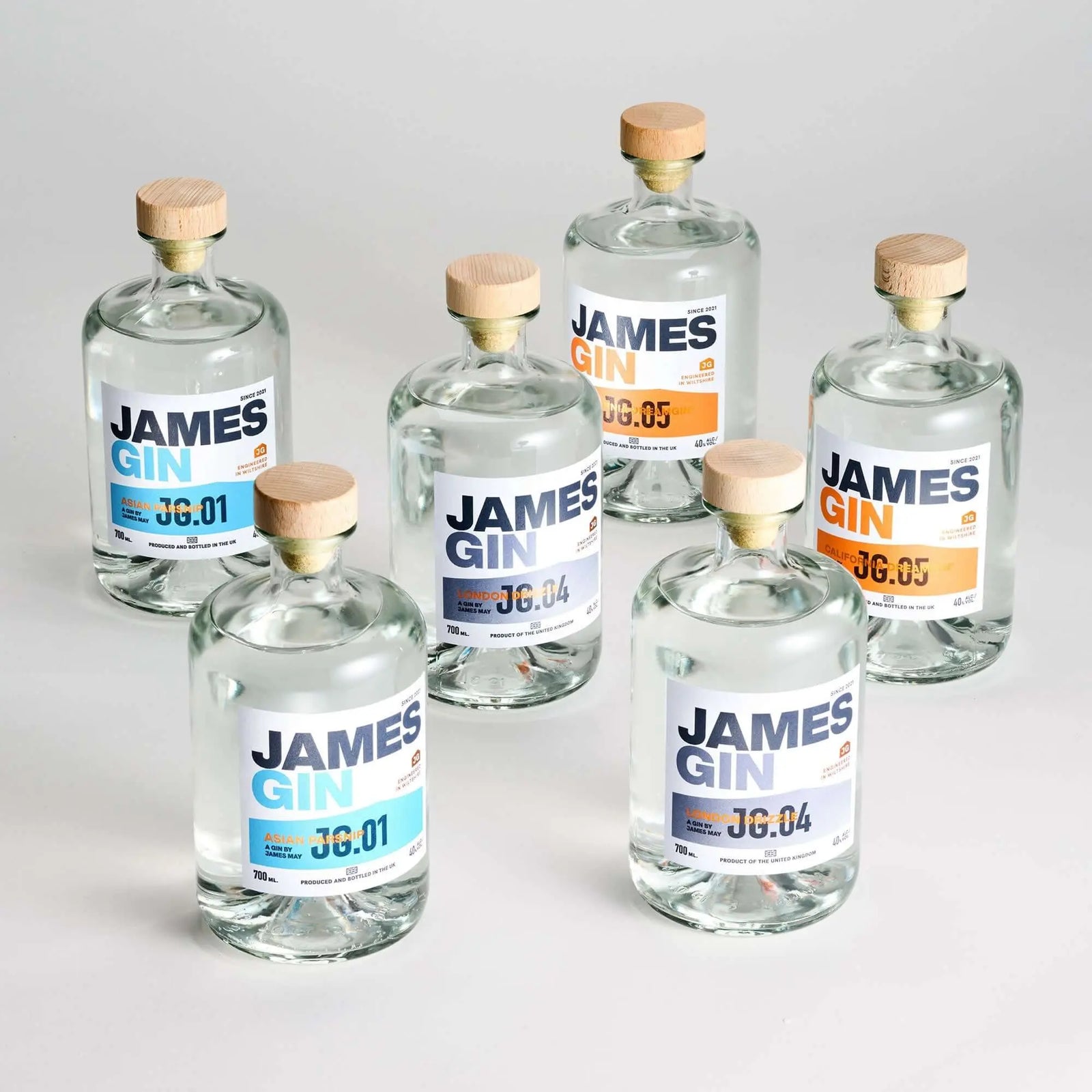 Discover the James Gin The Survivalist 6 Pack w/ Souvenir Gift Key Chain from James Gin US—six British craft gins with clear liquid, wooden caps, minimalist white labels with blue or orange accents, and unique batch numbers.