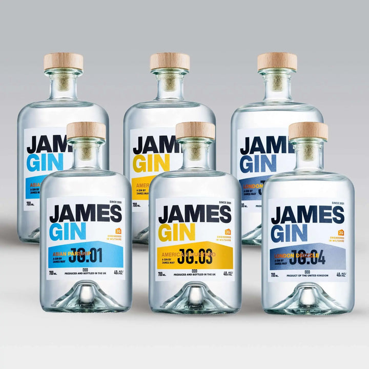 Five bottles from the James Gin The Collector Bundle with wooden caps are displayed on a light surface. Each clear bottle by James Gin shows batch numbers and blue or yellow highlights on labels, plus a souvenir gift key chain is included.