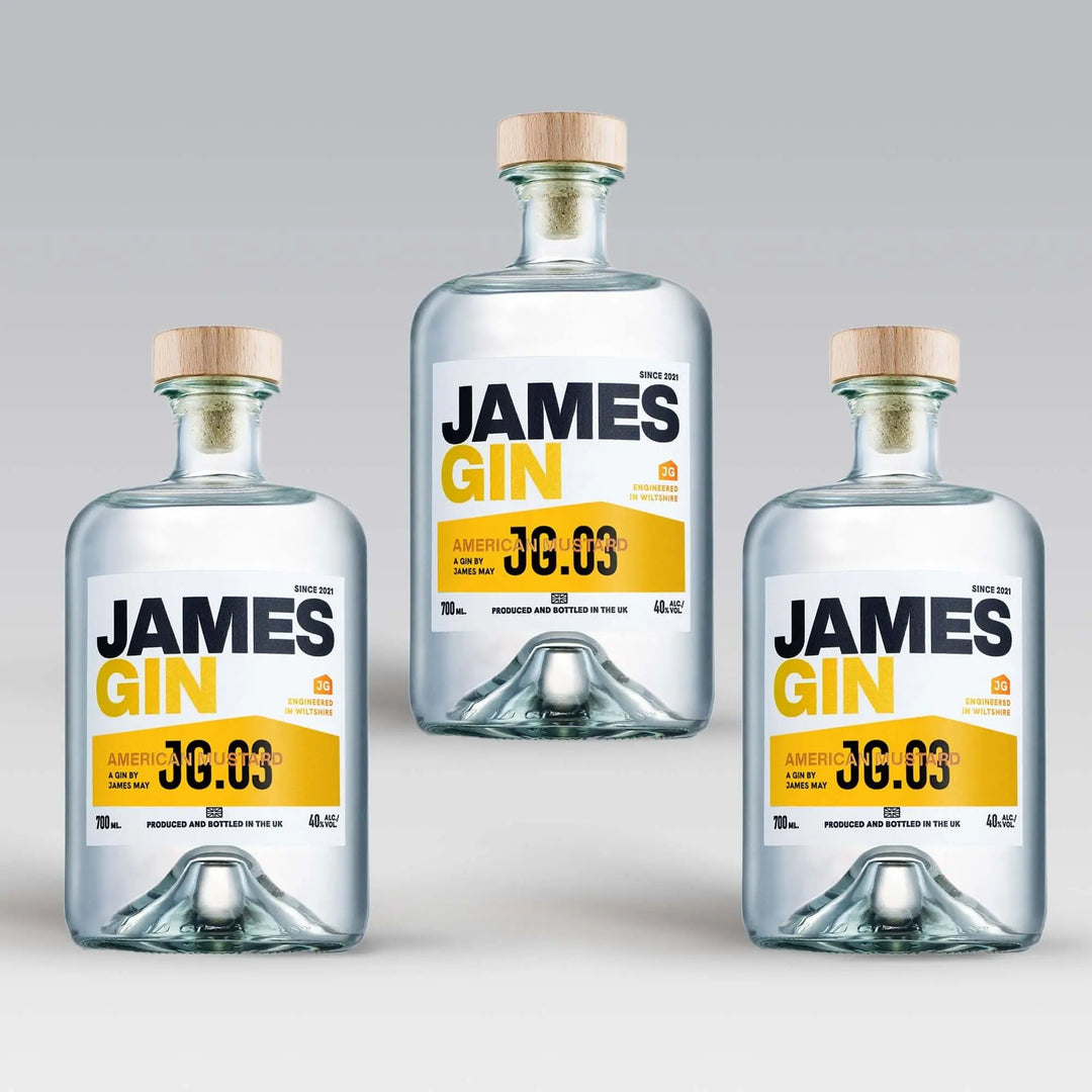 Three bottles of James Gin US "The Big, Beautiful Bundle" with wooden caps are arranged in a triangle on a light gray background. Each features a white label with bold black and yellow text, plus a souvenir gift key chain.
