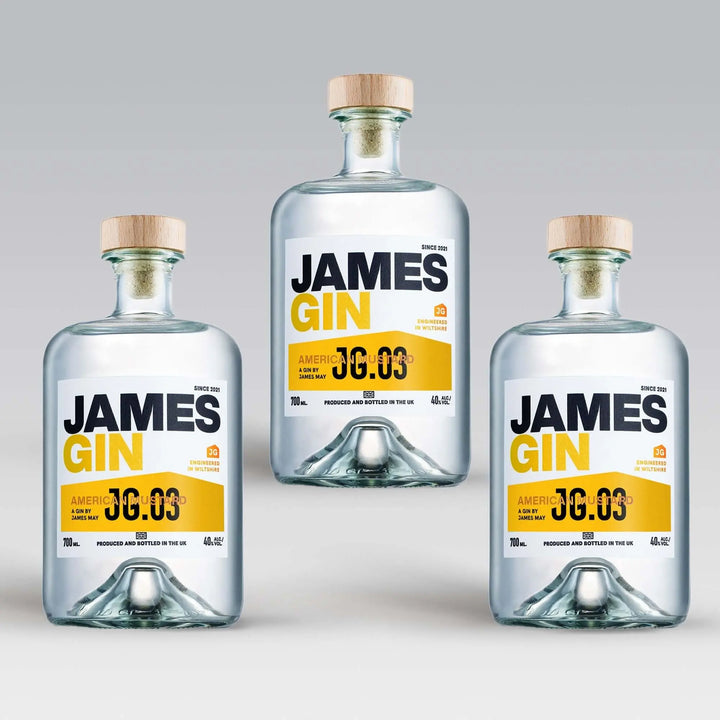 Three bottles of James Gin US "The Big, Beautiful Bundle" with wooden caps are arranged in a triangle on a light gray background. Each features a white label with bold black and yellow text, plus a souvenir gift key chain.