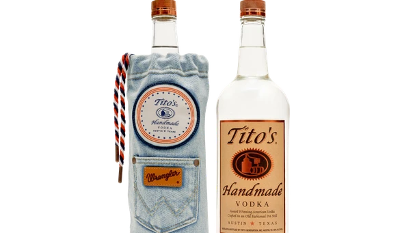 Two bottles of Tito's Vodka: one is the limited edition Tito's X Wrangler® 1L with a denim sleeve featuring a pocket and braided cord, making it collectible; the other reveals the full label.